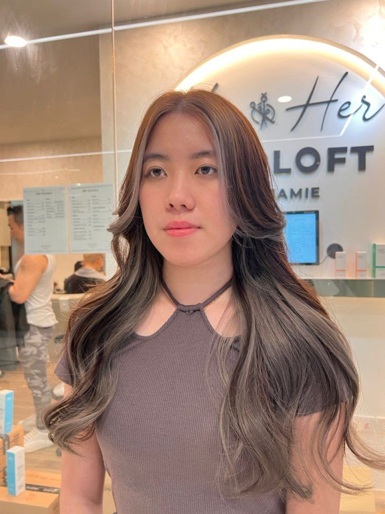 Client with long ash-brown waves in front of the Hairloft sign